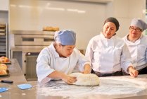 Шеф-повар обучает студентов с синдромом Дауна месить тесто — стоковое фото
