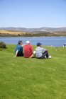 Golfistas masculinos fazendo uma pausa descansando na grama no campo de golfe ensolarado — Fotografia de Stock