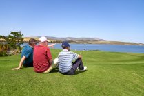Чоловіки гольфи розслабляються, дивлячись на озеро з сонячного поля для гольфу — стокове фото