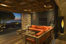 Illuminated modern, luxury home showcase sofa open to patio at dusk — стоковое фото