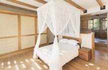 Білі марлеві штори на ліжко на балдахіні в сучасній, розкішній домашній вітрині інтер'єру спальні — стокове фото