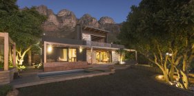 Berge hinter beleuchtetem modernem, luxuriösem Haus präsentieren Haus im Freien bei Nacht — Stockfoto