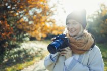 Усміхнена жінка з цифровою камерою в сонячному осінньому парку — стокове фото