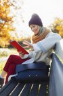 Young woman using digital tablet on autumn park bench — Stock Photo