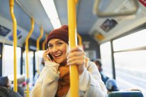 Усміхнена молода жінка розмовляє на смартфоні в автобусі — стокове фото