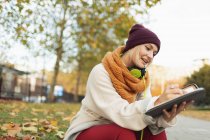 Young woman writing in journal in autumn park — Stock Photo