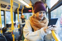 Mulher jovem em tampão de meia e cachecol usando tablet digital em ônibus — Fotografia de Stock