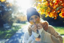 Портрет щасливої молодої жінки, що тримає осіннє листя в сонячному парку — стокове фото