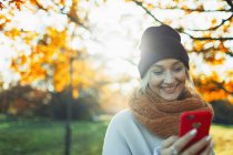 Sorrindo mulher com telefone inteligente no parque de outono ensolarado — Fotografia de Stock