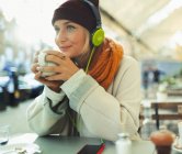 Young woman with headphones listening to music and drinking coffee at sidewalk cafe — Stock Photo