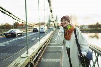 Young woman in stocking cap and scarf talking on smart phone on bridge — Stock Photo