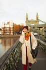 Молода жінка в панчішній шапці і шарфі розмовляє на смартфоні на міському мосту — стокове фото