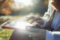 Feche a mulher usando tablet digital no parque de outono ensolarado — Fotografia de Stock
