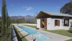 Idílico, piscina de luxo ensolarado e piscina casa com montanhas em segundo plano — Fotografia de Stock