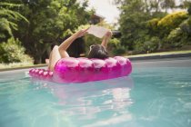 Женщина читает книгу о надувном плоту в солнечном летнем бассейне — стоковое фото