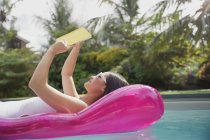 Жінка читає книгу на надувній плоті в сонячному літньому басейні — стокове фото