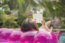 Женщина расслабляется, читает книгу о надувном плоту в бассейне — стоковое фото