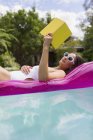 Женщина расслабляется, читает книгу о надувном плоту в летнем бассейне — стоковое фото