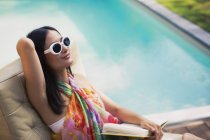 Спокойная женщина расслабляется, читает книги у бассейна летом — стоковое фото