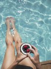 Frau entspannt sich, taucht barfuß in sommerliches Schwimmbad und isst Beeren aus Kokosnuss — Stockfoto