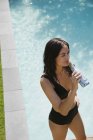 Woman in bikini drinking water at sunny summer poolside — Stock Photo