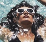 De cerca mujer serena en gafas de sol relajante, flotando en la piscina soleada de verano - foto de stock
