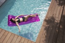 Heitere Frau entspannt sich auf aufblasbarem Floß im sonnigen Sommerschwimmbecken — Stockfoto