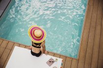Mulher de chapéu de sol e biquíni relaxante à beira da piscina — Fotografia de Stock