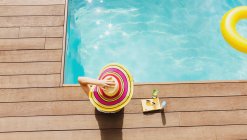 Chapeau femme au soleil relaxant au bord de la piscine ensoleillée — Photo de stock