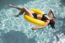 Чуттєва жінка в бікіні плаває на жовтому надувному кільці в сонячному басейні — стокове фото