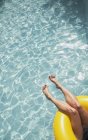 Жінка з голими ногами розслабляється, плаває в надувному кільці в сонячному басейні — стокове фото