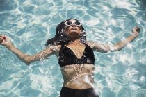 Mulher serena de biquíni preto flutuando na piscina ensolarada de verão — Fotografia de Stock