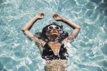 Serene woman floating in sunny summer swimming pool — Stock Photo