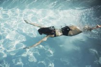 Mulher de biquíni nadando subaquático na piscina ensolarada — Fotografia de Stock