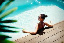 Mulher relaxante com coquetel na piscina ensolarada de verão — Fotografia de Stock