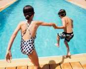 Junge und Mädchen halten Händchen und springen in sonniges Sommerschwimmbecken — Stockfoto