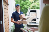 Smiling deliveryman watching woman signing smart phone at front door — Stock Photo