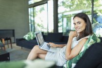 Retrato confiante empresária trabalhando em casa, usando laptop na sala de estar — Fotografia de Stock