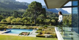 Femme debout sur un balcon ensoleillé et luxueux donnant sur la piscine et le paysage, Le Cap, Afrique du Sud — Photo de stock
