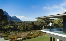Woman standing on sunny, modern luxury balcony overlooking garden and mountains, Cape Town, South Africa — Stock Photo
