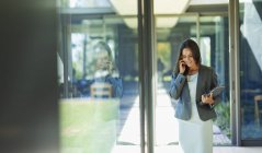 Бізнес-леді розмовляють по смартфону в сонячному коридорі — стокове фото