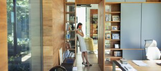 Mujer de negocios hablando por teléfono inteligente en el pasillo de la oficina en casa - foto de stock