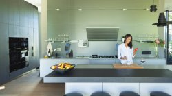 Donna con smart phone mangiare in cucina moderna — Foto stock