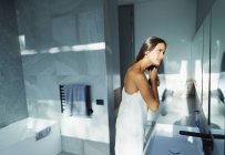 Donna avvolta in asciugamano spazzolare i capelli in bagno moderno — Foto stock