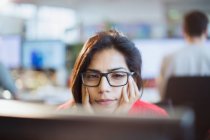 Сфокусированная деловая женщина с головой в руках, работающая за компьютером в офисе — стоковое фото