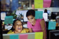 Femmes d'affaires heureuses utilisant l'ordinateur derrière des notes adhésives dans le bureau — Photo de stock