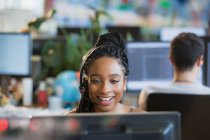 Donna d'affari sorridente con auricolare che lavora al computer in ufficio — Foto stock