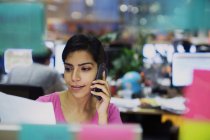 Geschäftsfrau telefoniert mit Smartphone und liest Papierkram im Büro — Stockfoto
