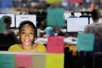 Уверенная в себе, улыбающаяся деловая женщина с наушниками, работающая за компьютером за клейкими нотами в офисе — стоковое фото