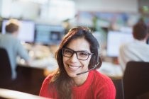 Портрет уверенный, улыбающаяся деловая женщина с наушниками работает в офисе — стоковое фото